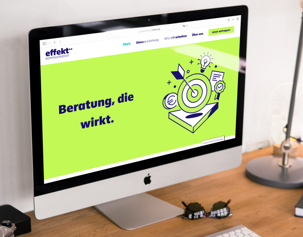 Ein Schreibtisch mit einem iMac. Auf dem Bildschirm ist die Startseite der Werbsite zu sehen.