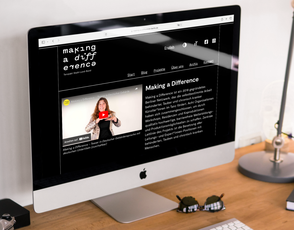 Ein Schreibtisch mit einem iMac. Auf dem Bildschirm ist die Startseite im Dark-Modus zu sehen.