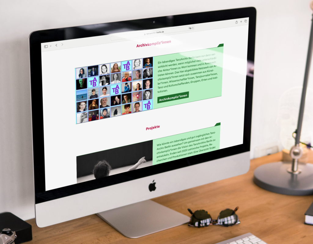 Ein iMac steht auf einem Schreibtisch. Auf seinem Bildschirm sind die Archivkompliz*innen zu sehen.